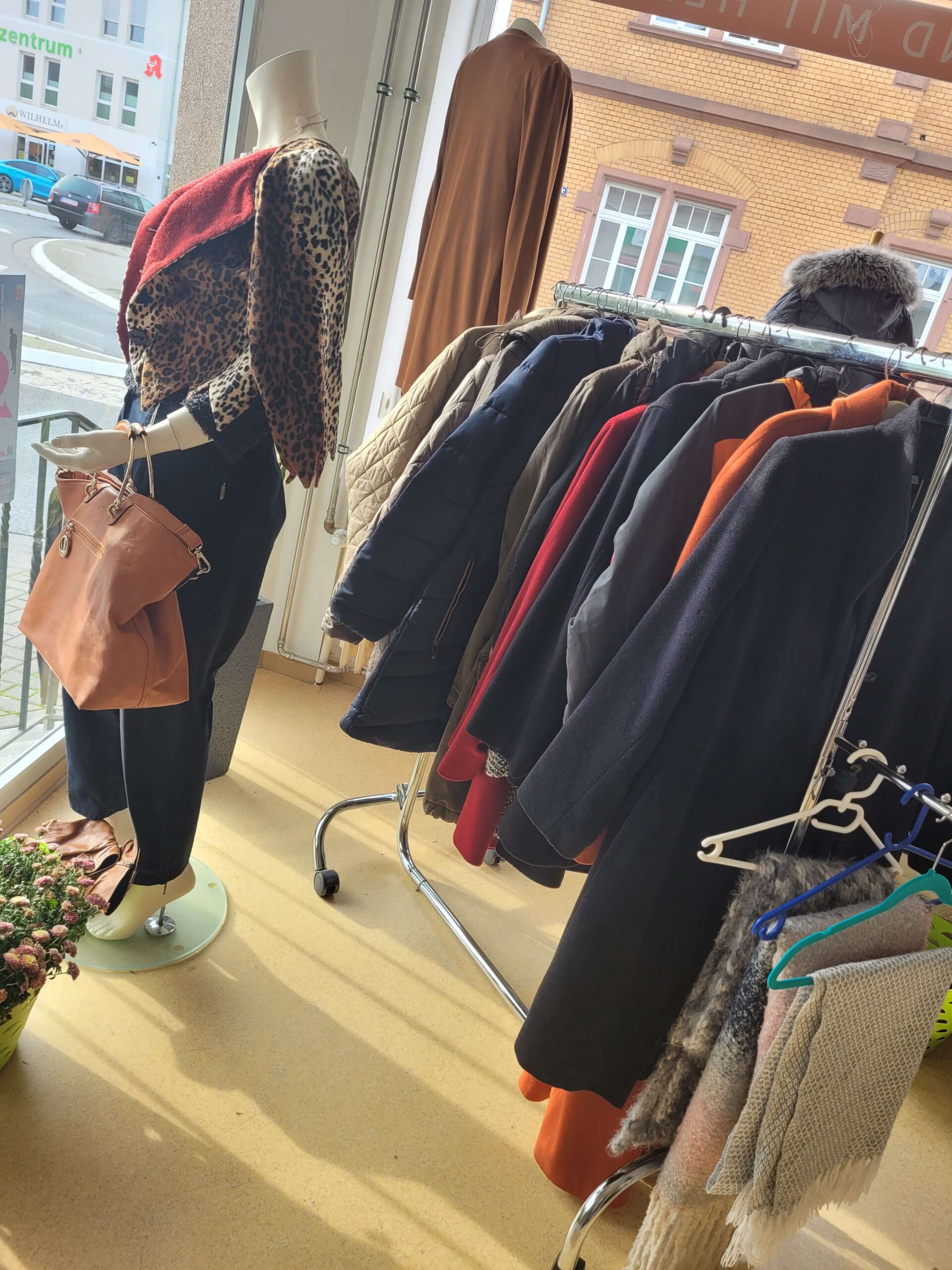 Kleiderständer mit eleganten Jacken vor einem großen Fenster im Second-Hand-Laden