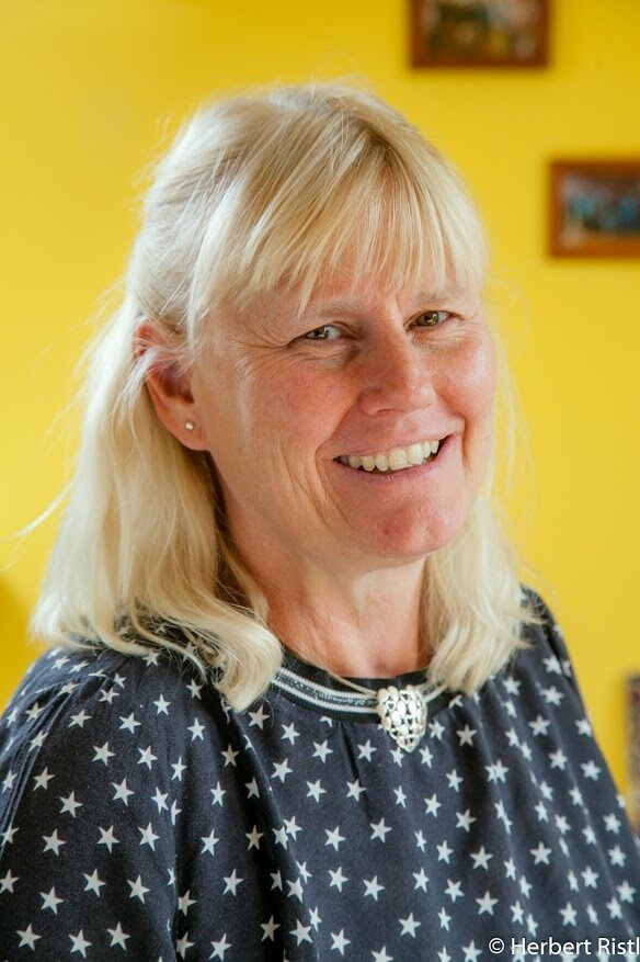 Blonde Frau mit silberner Herz-Kette, lächelnd im Fokus.