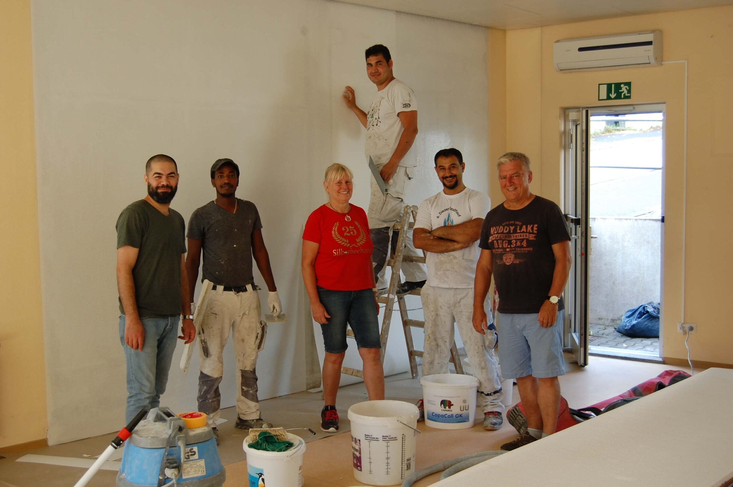 Gruppe von Menschen renoviert einen Raum, Farbeimer im Vordergrund